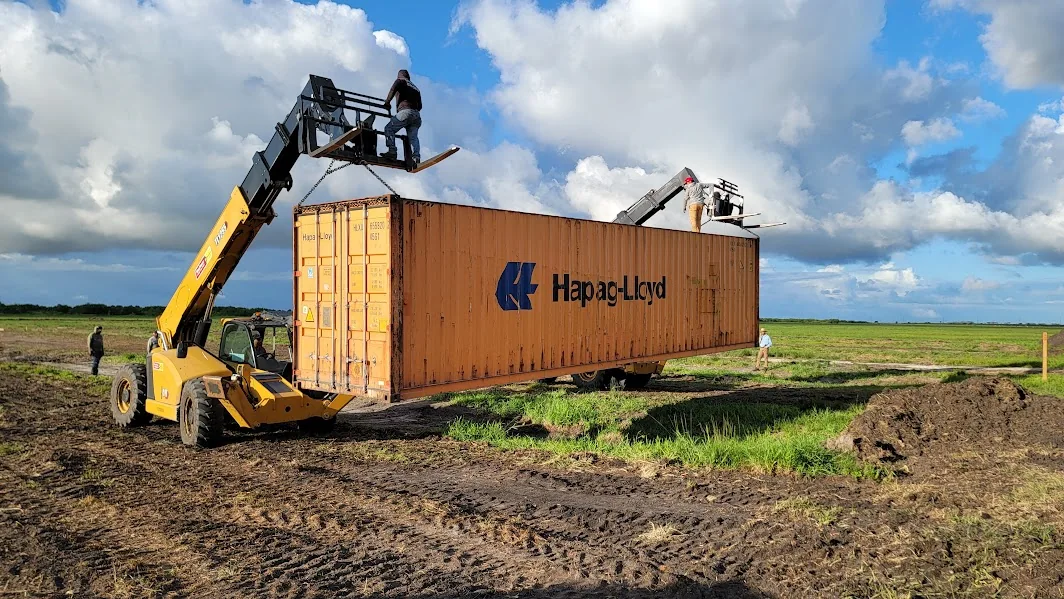 Orange shipping container being moved with heavy lifting equipment.